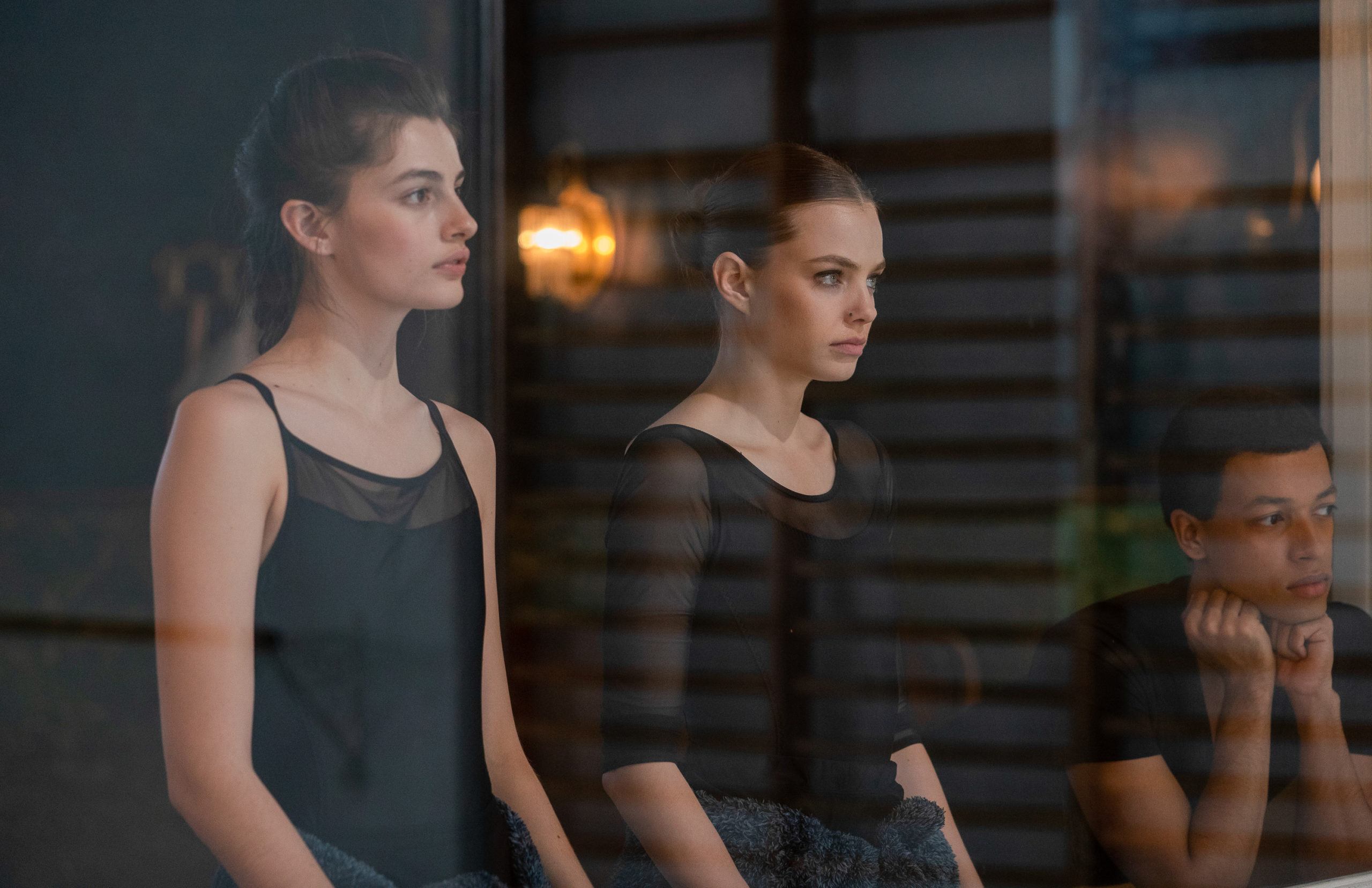 Diana Silvers and Kristine Froseth, wearing black leotards, look through a dance studio window.