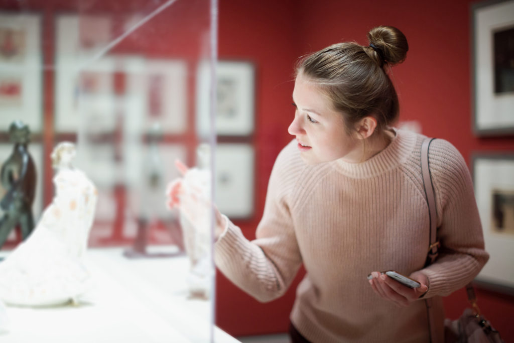 Young woman visitor looks at a small sculpture behind a glass case at a historical museum