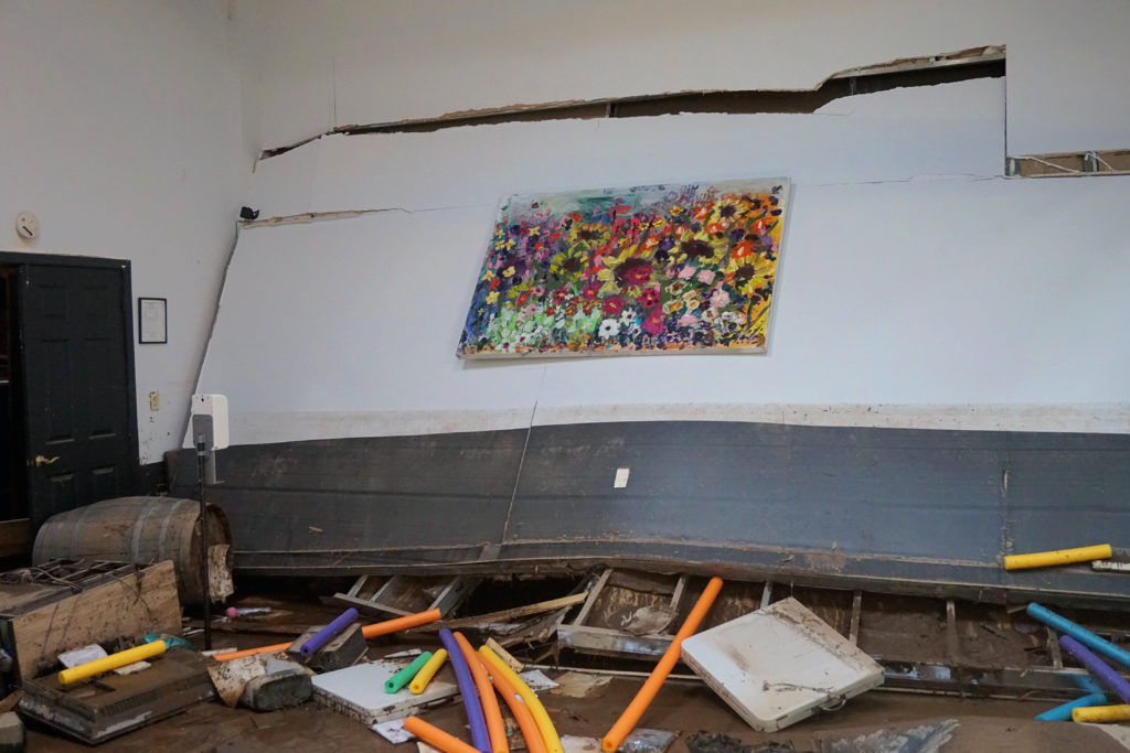 A dance studio is shown in shambles, with mud coating the floor, debris strewn everywhere, and the studio wall dislodging from the ceiling.