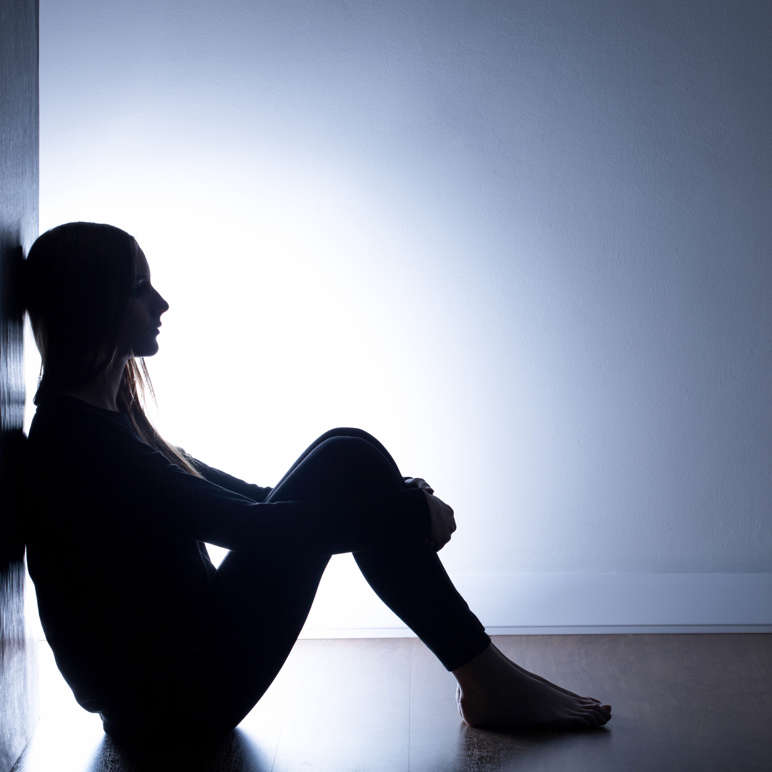 A teenage girl is shown in silhouette, sitting alone in dark room.
