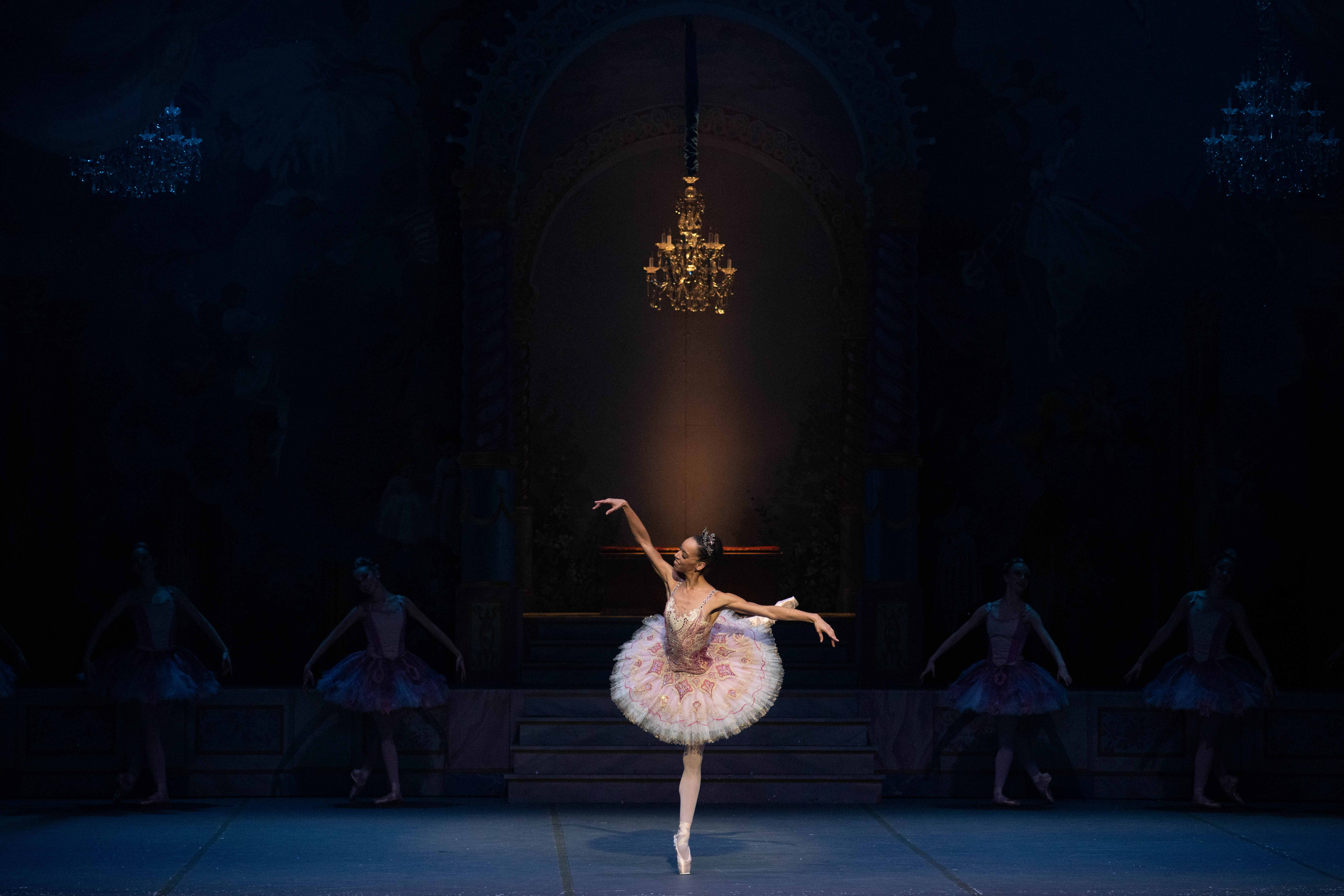 Chyrstyn Fentroy stands onstage against a black backdrop in a pink tutu. She is in attitude derriere, facing front.
