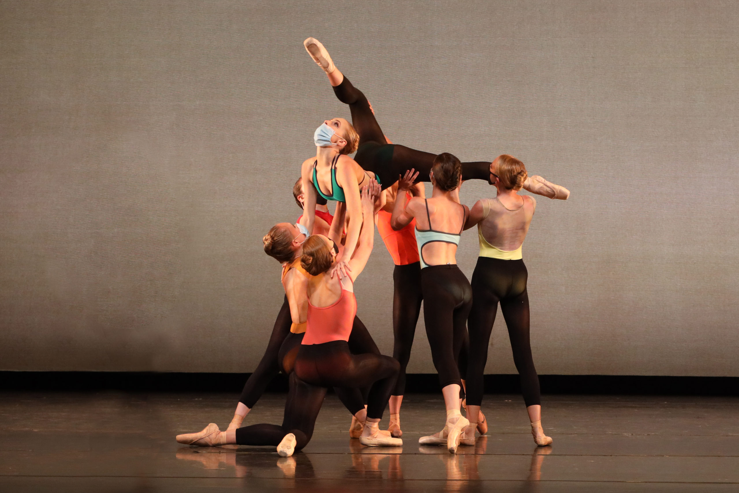 Five young adult dancers suspend and support Emmanuelle Watkins overhead as she arches backwards, her legs split in the air.
