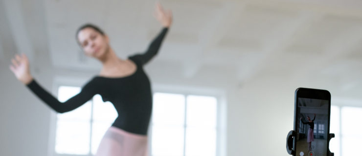 Young ballerina dancing ballet and shooting her performance on mobile phone in a dance studio.