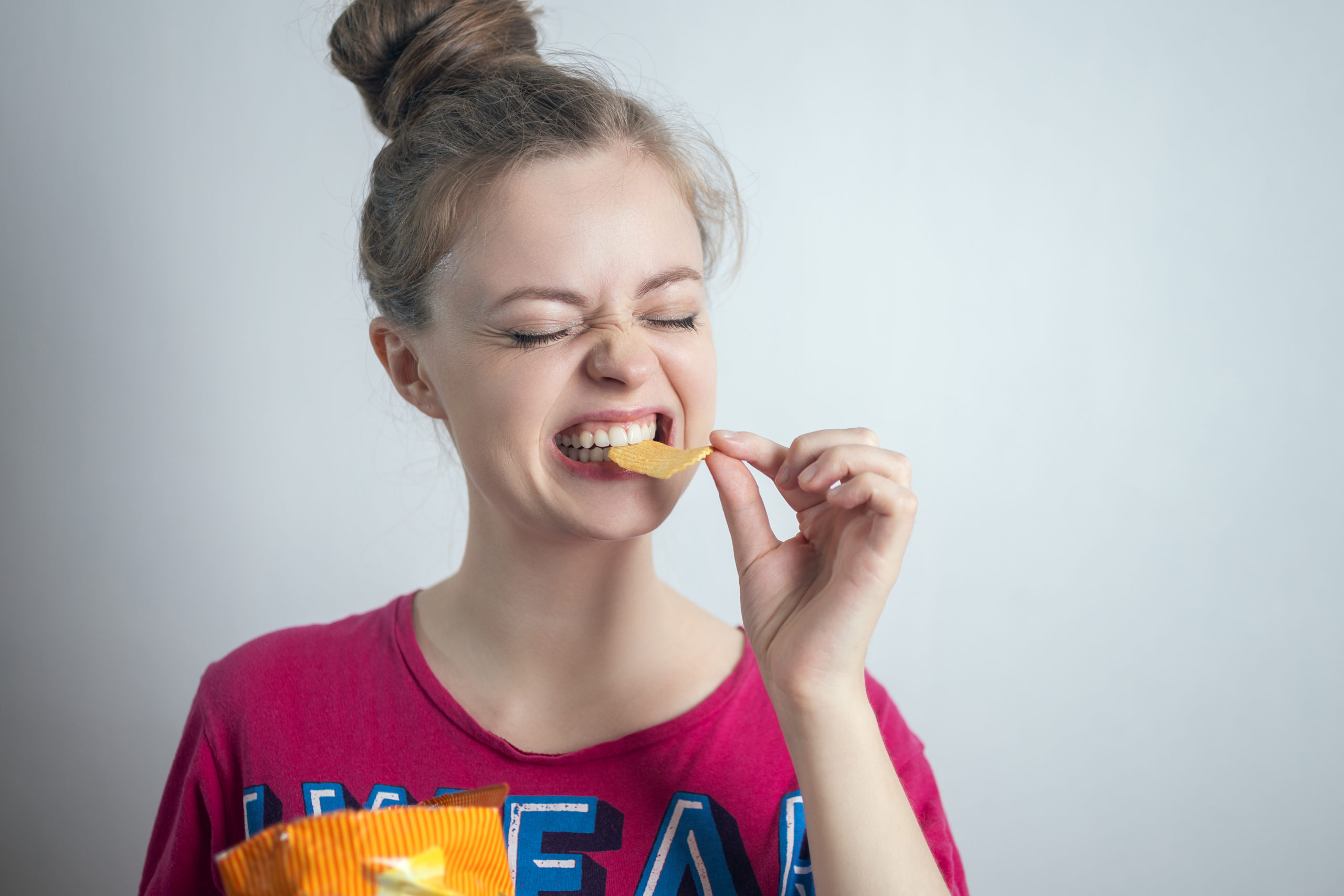 Smiling young Caucasian woman girl eating biting potato chips