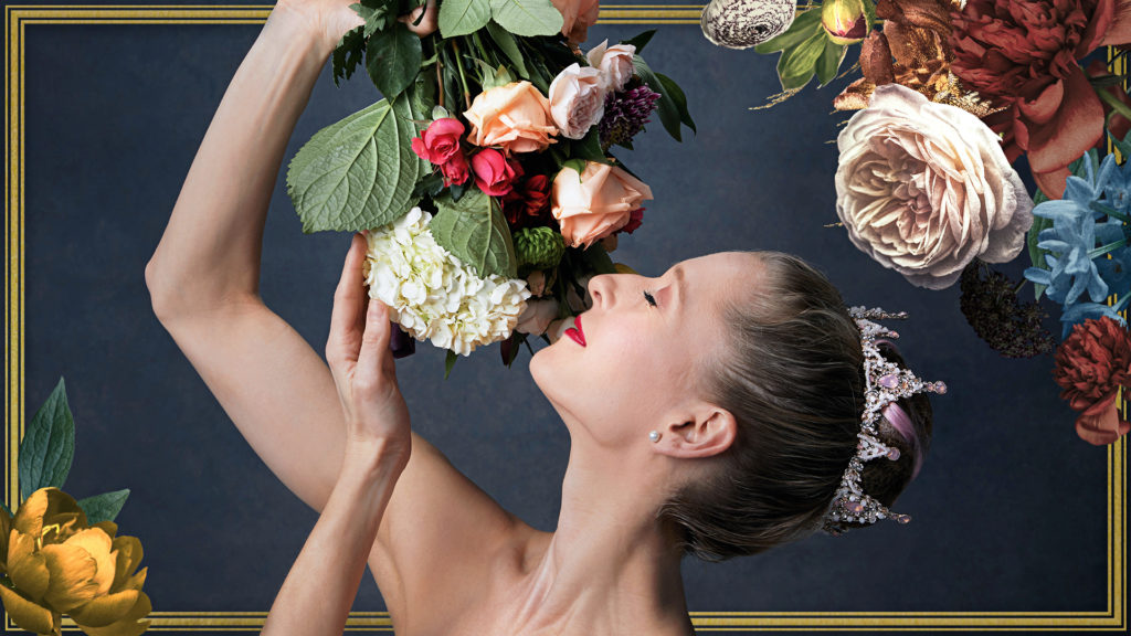 A ballerina is photographed from the shoulders up in a promotional ad for the ballet "The Sleeping Beauty." She wears a jeweled tiara around her high bun, and reaches up to smell a bouquet of flowers that hangs down towards her face. She closes her eyes as if taking in the small of roses.
