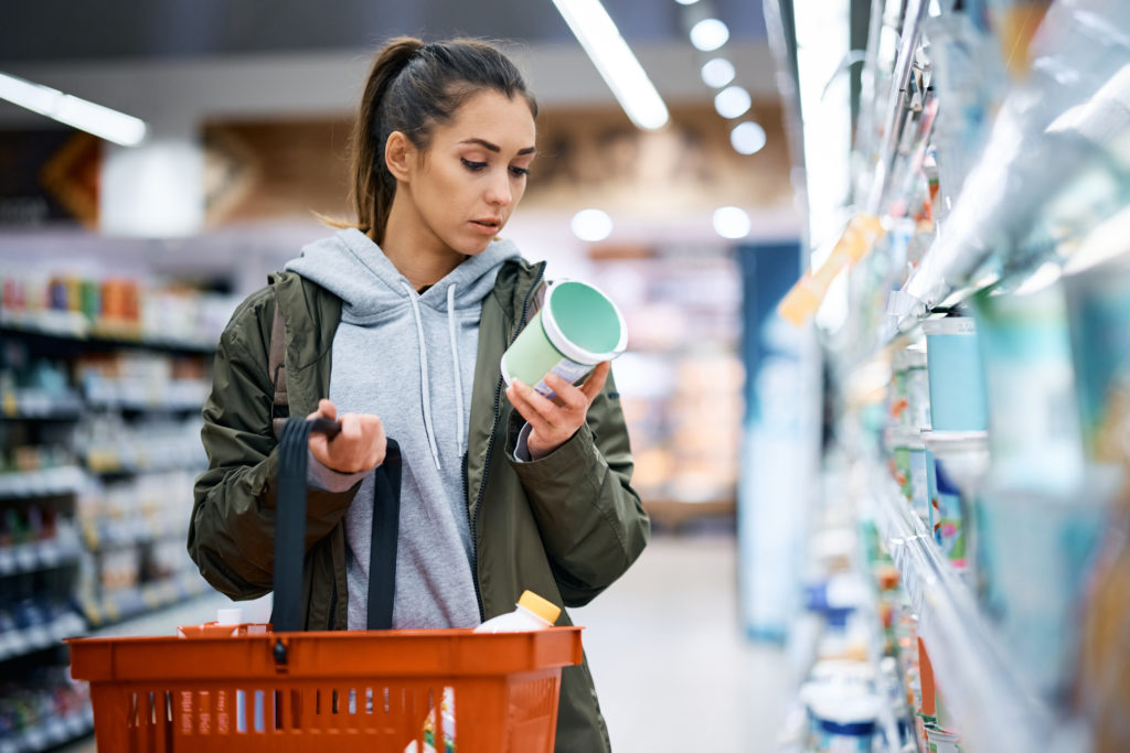 Young woman buying dairy product and reading food label in grocery store.