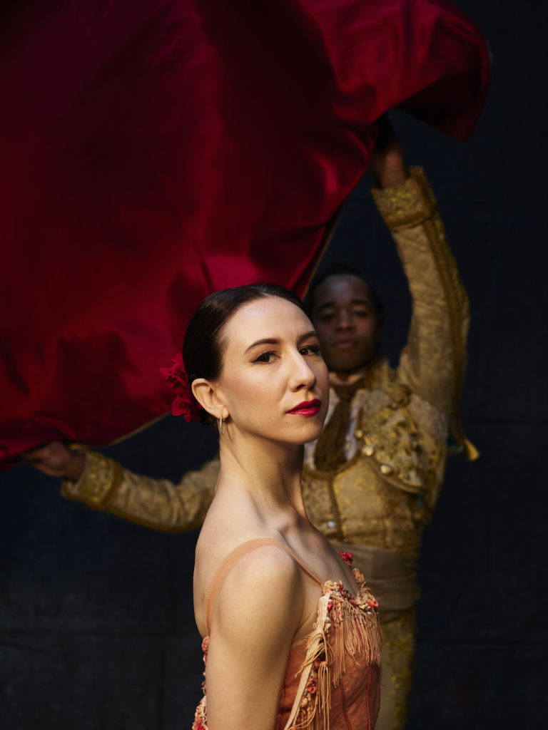 Isabella Boylston and Gabe Stone Shayer are in costume for Don Quixote. Boylston, foreground, looks at the camera over her right shoulder. Shayer, background, raises a red cape.