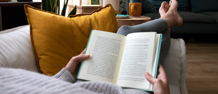 Point of view of a young woman relaxing at home reading a book while lying on sofa.