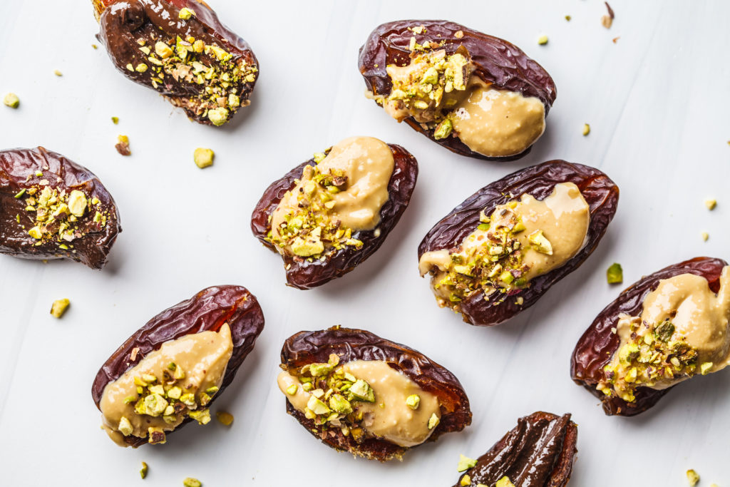 Nine dates stuffed with nut butter and crushed pistachios sit on a white background.