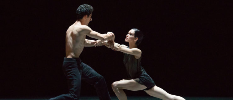 Tigran Sargsyan and Petra Conti firmly grasp each other's forearms, arms crossed as they gaze into each other's eyes. Conti is in a low lunge, her right leg extended back with pointed toes.