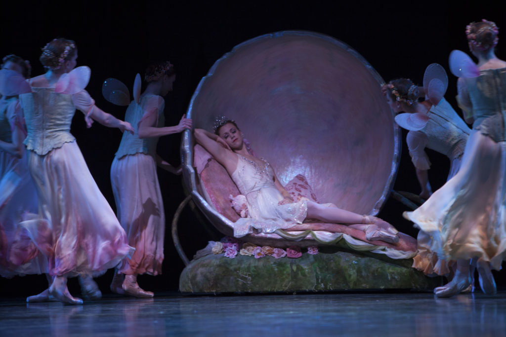 Titania elegantly reclines in a large pink shell. She is asleep while fairies dance around her.