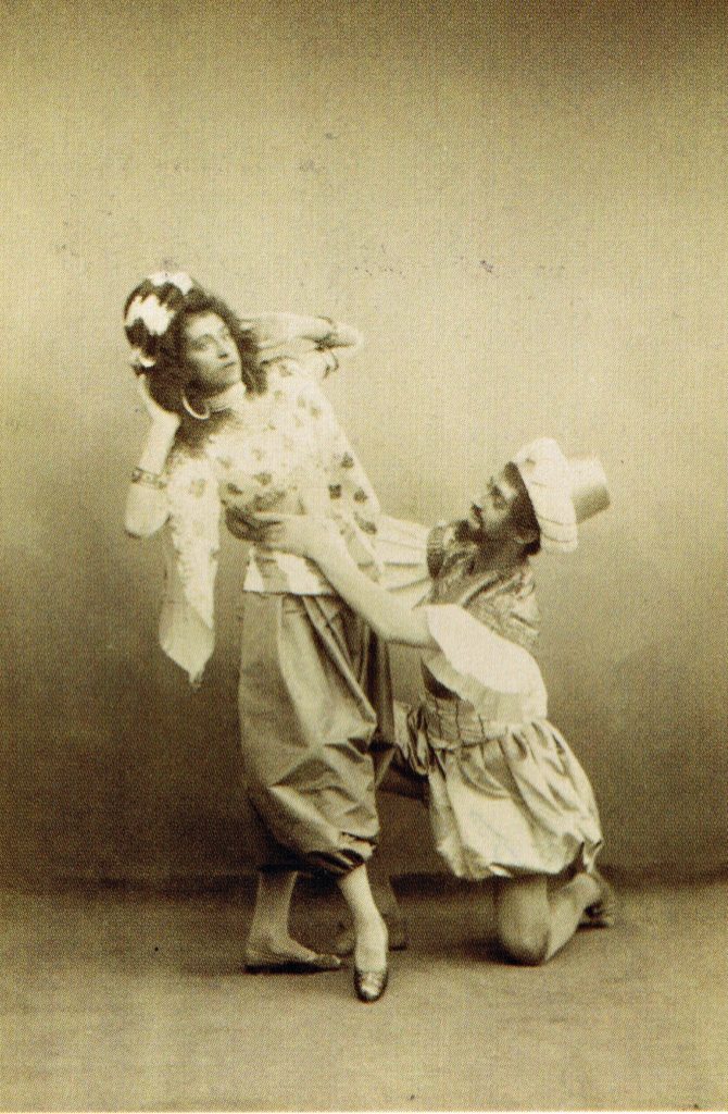 Skorsiuk (standing) and Gorsky (kneeling, holding Skorsiuk's waist) pose in costume for Raymonda's saracen dance. The photograph is old and sepia-toned.