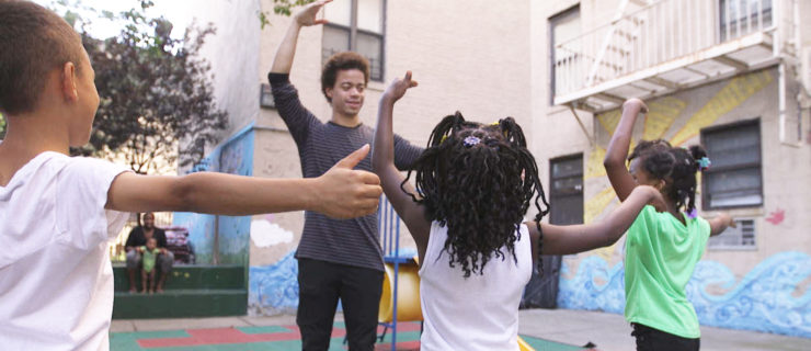 Steven Melendez shows three young children a dance move outside on a playground.