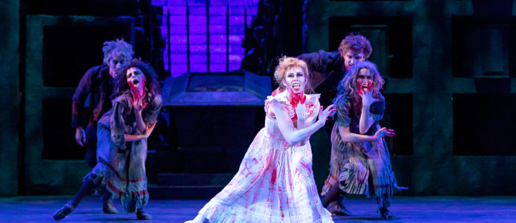 Jennifer Grace, in a long white dress stained with fake blood, dances onstage in front of a dark gated garden setting. She has darkened eye makeup, messy hair and fake bloodstains on her face and hands as she sneers at the audience, mouth wide open as if to lick the blood off of her hands. Two pairs of dancers, one male and one female per pair, dressed in darker colors mimic her movement and are also covered in fake bloodstains.