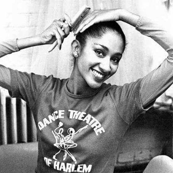 Julie Felix, then a DTH member, brushes her hair while smiling at the camera. She is wearing a T-shirt that reads, "Dance Theatre of Harlem." The image is in black and white.