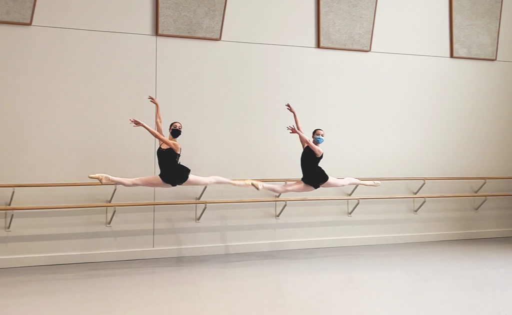 Two ballet dancers photographed in the air in split leaps.