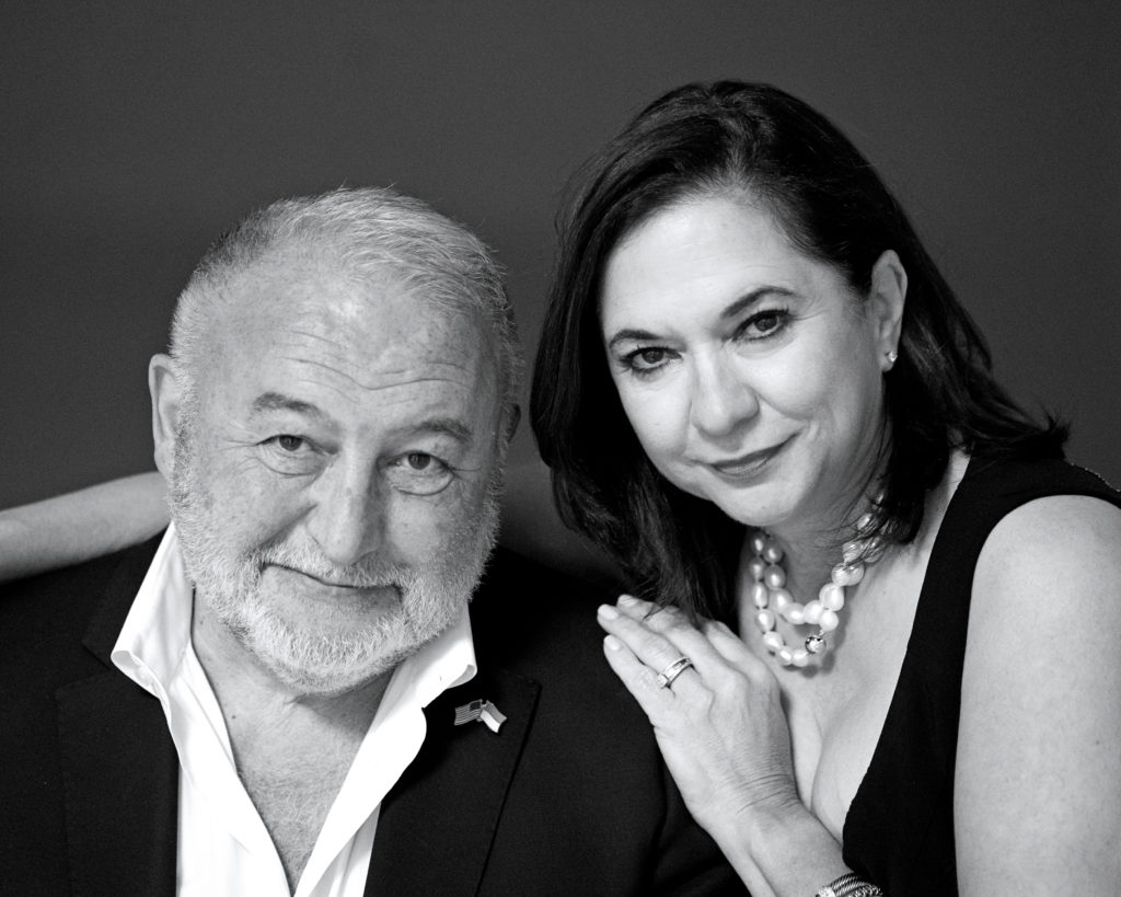In this black and white photo, Michael Krasnyansky and Gladisa Guadalupe are shown from the chest up, smiling towards the camera. Krasnyansky wears a white shirt with an open collar and a black sport coat. Guadalupe, wearing a low-cut black top and pearl necklace, puts her right arm around his left shoulder and her left hand on his left shoulder.