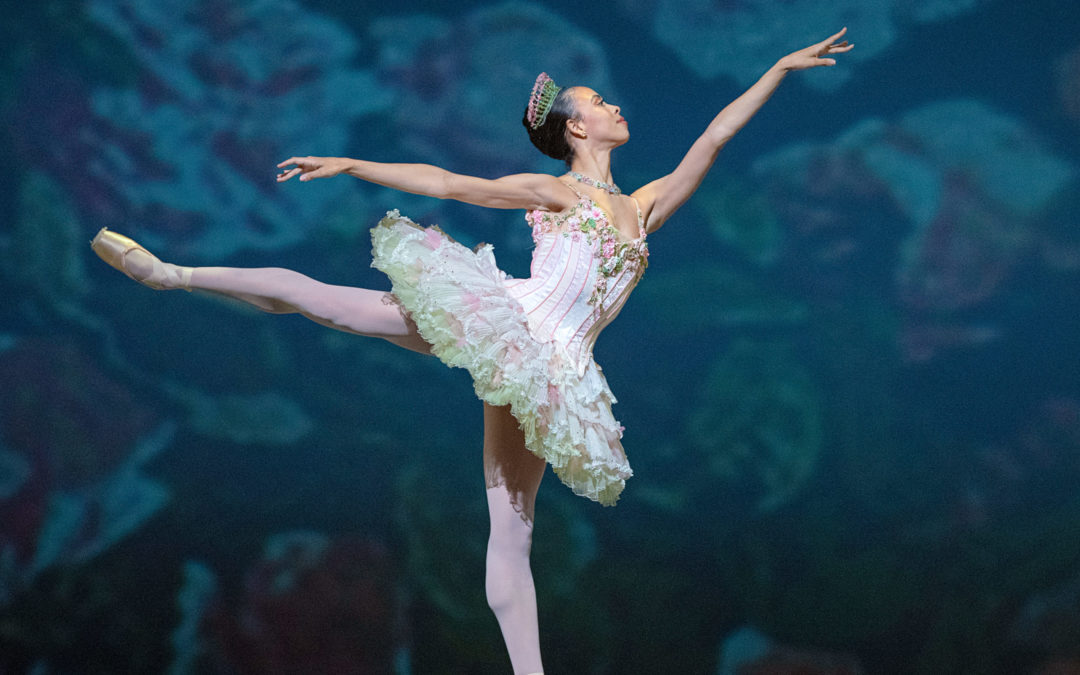 During a performance of "The Nutcracker," Nikisha Fogo does a first arabesque on pointe with her right leg up. She wears a light pink tutu with green trim and small flowers along the bodice, and a pink and green tiara, pink tights and pointe shoes.
