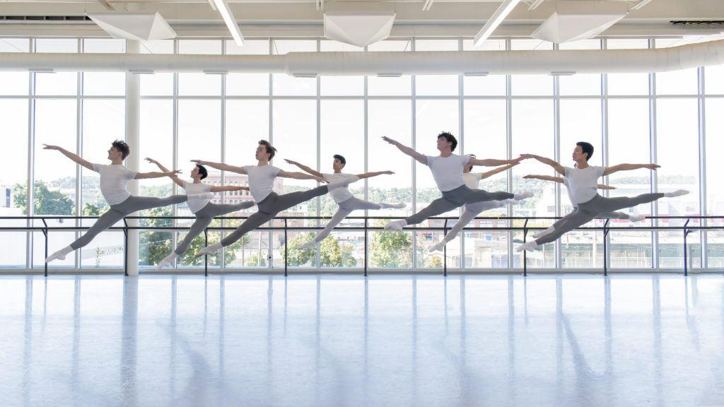 A group of young men photographed mid-leap in a ballet studio.