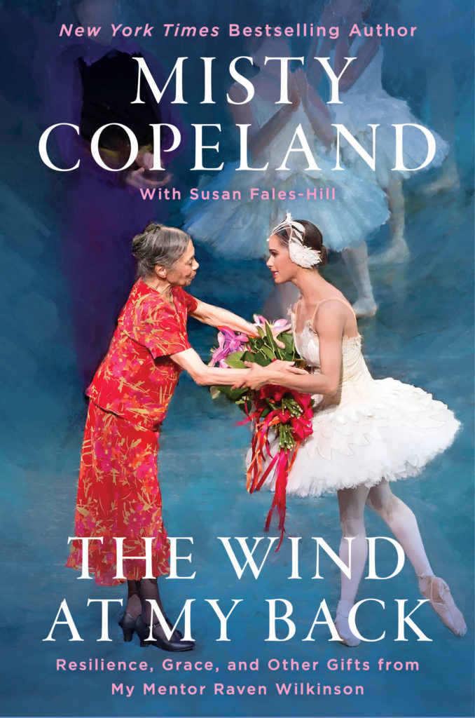 A book cover. Misty Copeland, in an Odette costume (white tutu, headpiece, ballet tights and pointe shoes), accepts a bouquet of flowers from Raven Wilkinson, who wears a red dress. White text reads "Misty Copeland" and "The Wind at My Back"