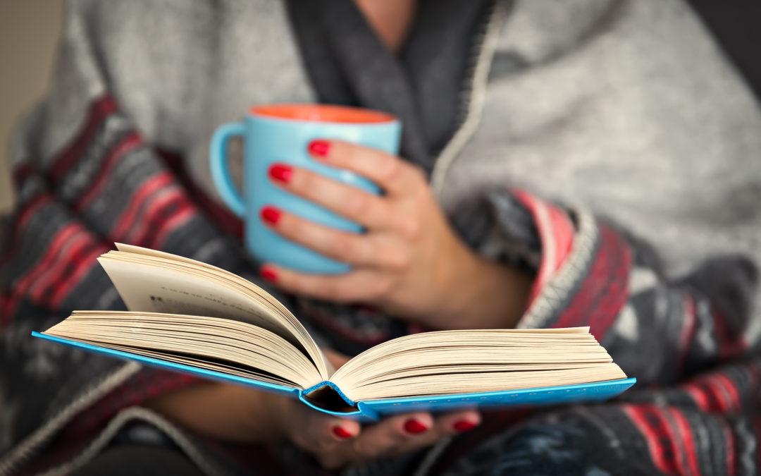 woman reading a book and holding a mug of hot beverage