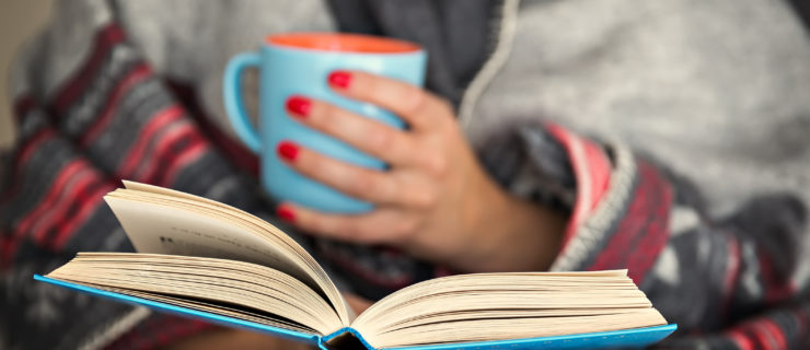 woman reading a book and holding a mug of hot beverage