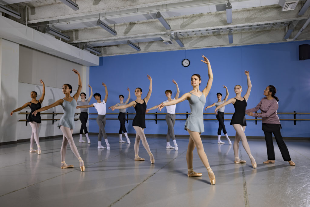 A class of male and female ballet students in tendu devant.