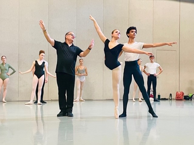 A male teacher coaches a teen couple in a ballet partnering class.