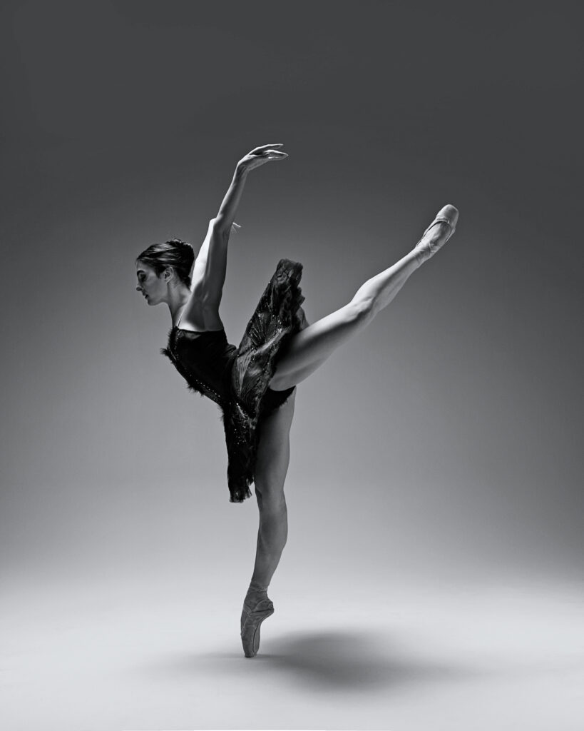 Tara Ghassemieh is in attitude en pointe, wearing a black tutu. The photo is in black and white.