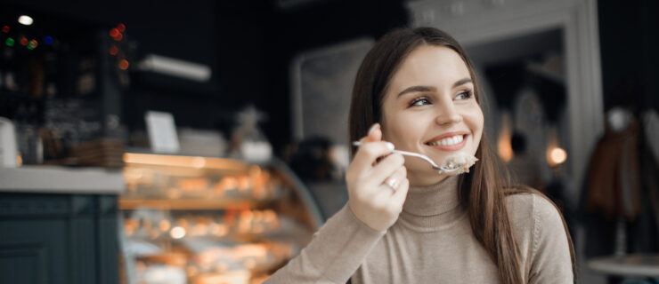 Teen girl with long, dark hair smiling while having a bite of cake and a hot beverage in a café.