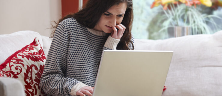 A teen girl bites her fingernails as she anxiously looks at her laptop.