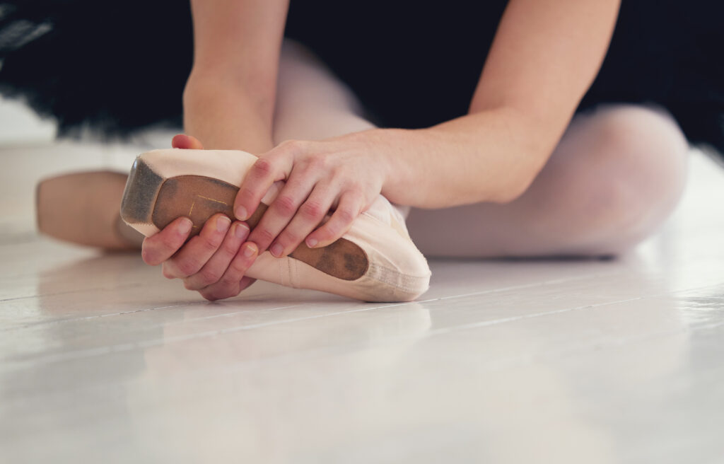 A ballet dancer rubs an aching foot in a pointe shoe.