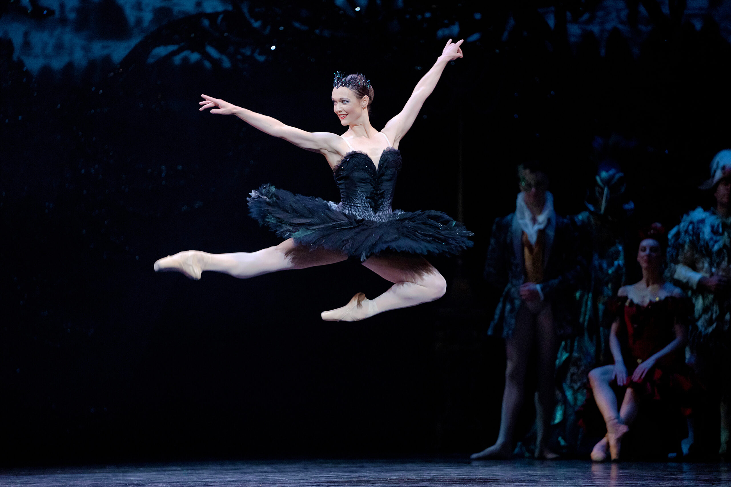 Jurgita Dronina, in a black feathered tutu as Odile, is photographed in the air mid-leap, her right leg extended in second and her left leg bent under her torso.