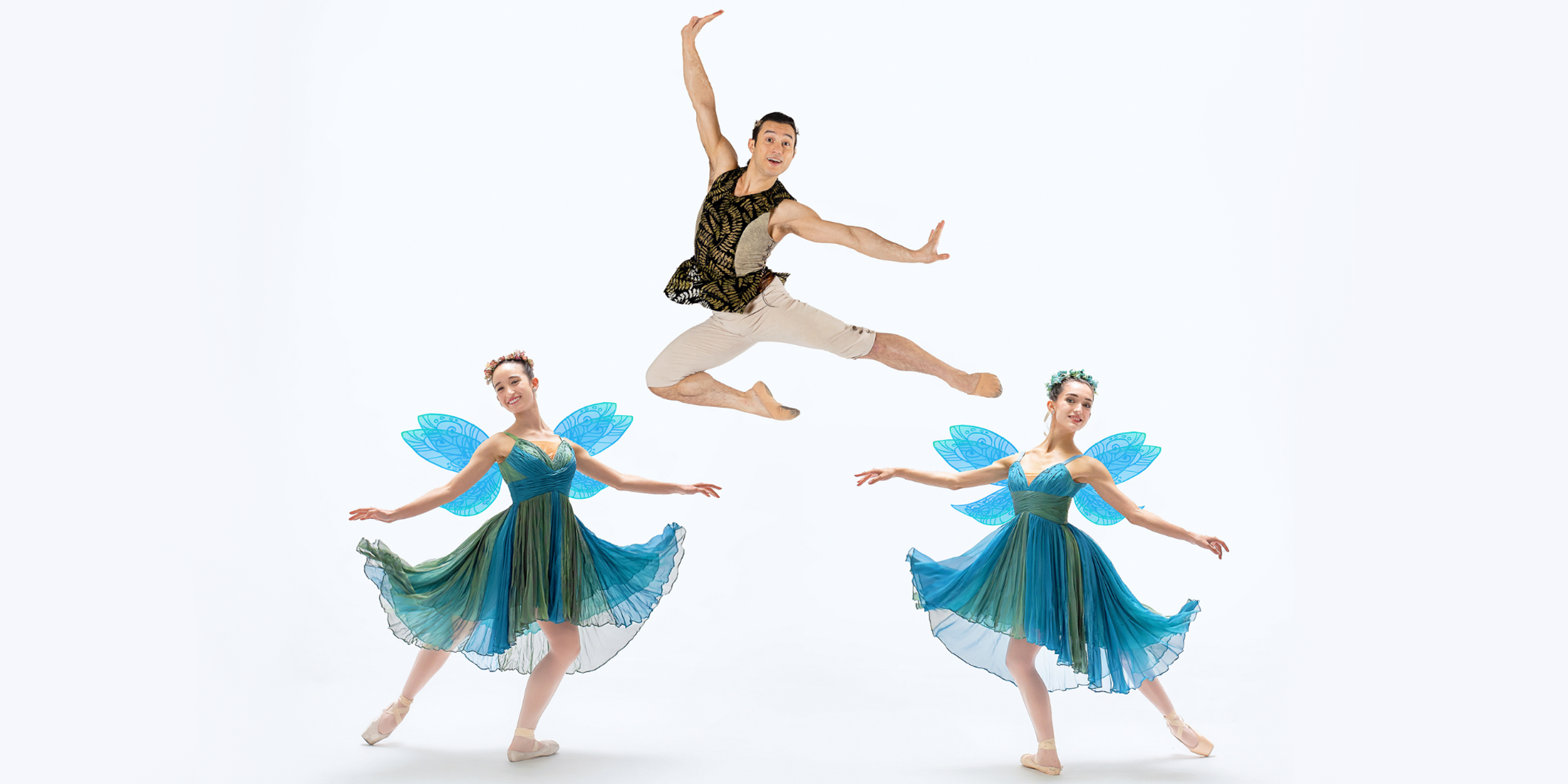In front of a blank white background, two female dancers dressed as fairies and one male dancer pose for a photo. The fairies, wearing blue and green dresses with blue wings, pose in tendu efface derriere, mirroring each other. The male dancer wears a brown vest and tan tights, leaping in a stylized Italian pas de chat.