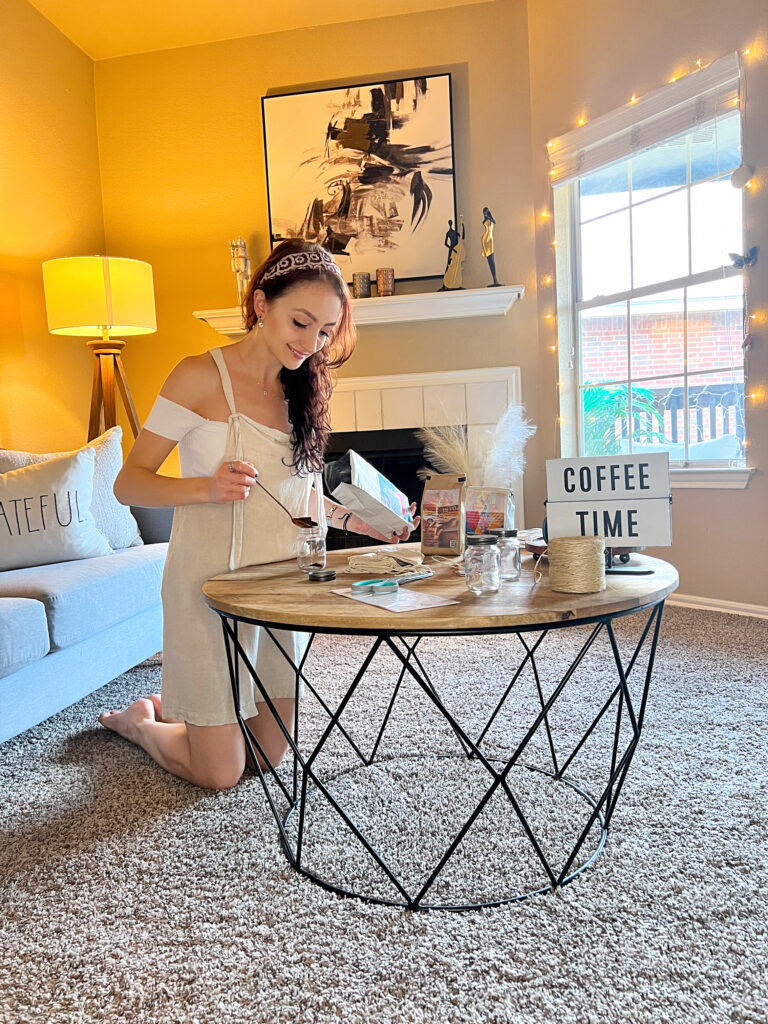 Buse Babadag spoons ground coffee into a jar in a living room. She is kneeling next to a coffee table. On the table is a sign that reads, "Coffee time."