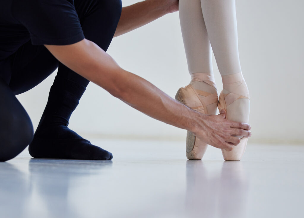 Closeup shot of a ballet teacher assisting a student with her position in a dance studio