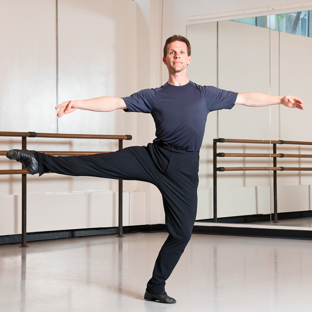 Daniel Ulbricht demonstrates the plié between à la seconde turns. He is in a ballet studio and wearing a black T-shirt with black pants and shoes.