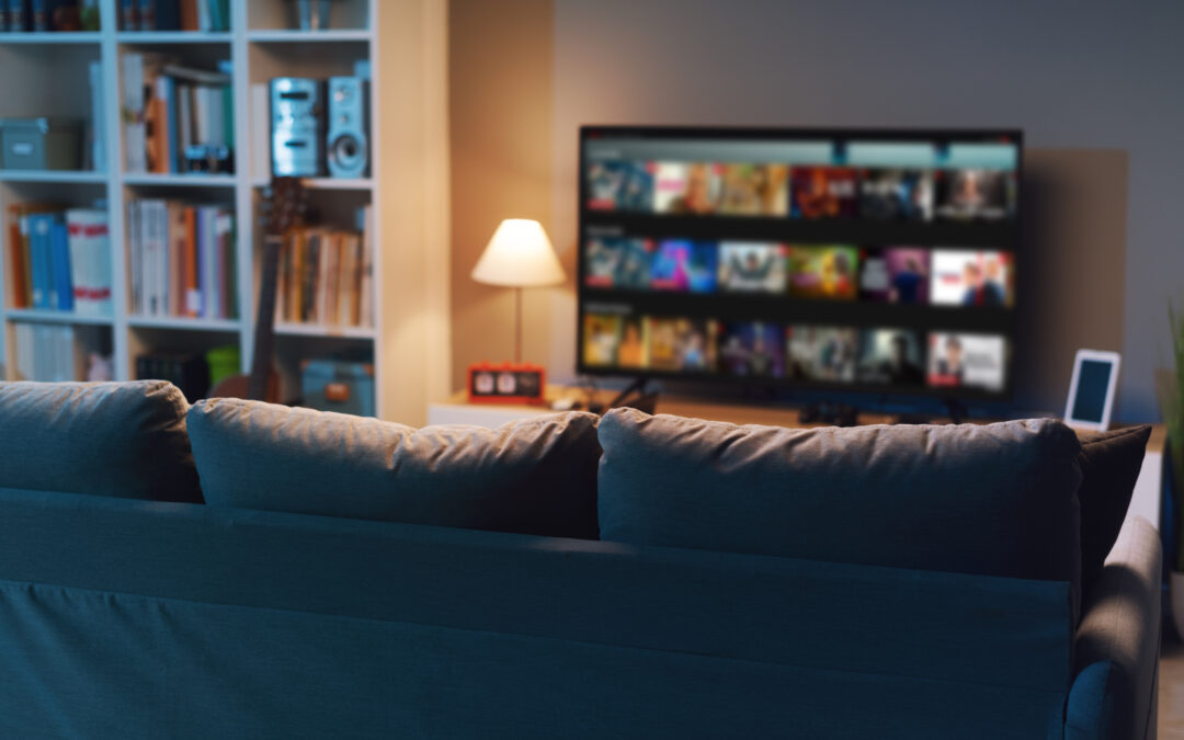 The back of a dark blue couch in a living room. In the background against the wall is a smart TV with video on demand menu on the screen.