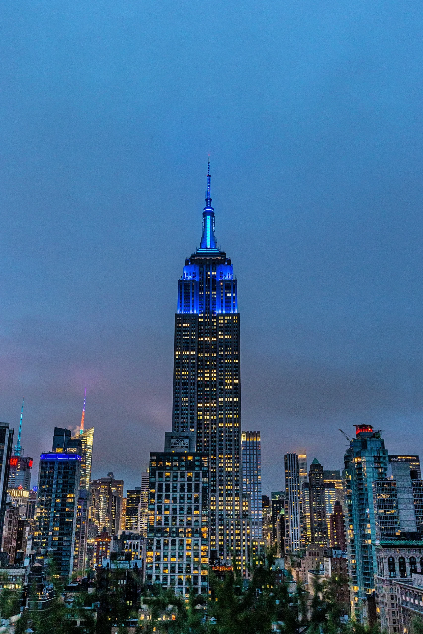 The Empire State Building lit in "Balanchine Blue" in front of an NYC evening skyline.