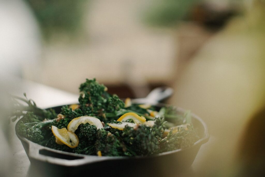 A bowl of broccolini with lemon wedges rests on a table.