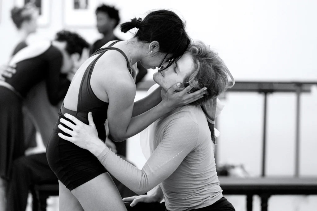 Jenna Savella and Harrison James in rehearsal for Emma Bovary. They dance an emotional pas de deux together in a dance studio; she cradles his head in her hands, and he rests his hand on her hip.