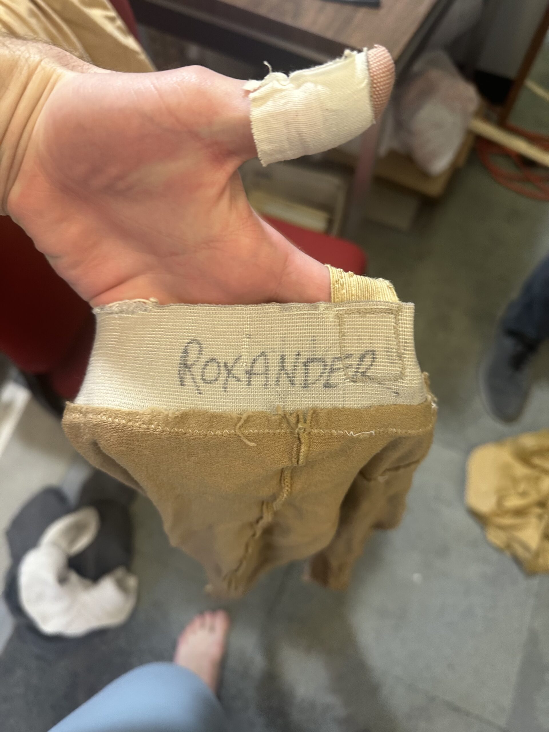 A close-up photo of Ashton Roxander's hand holding a old pair of light brown tights in his hand, the name "Roxander" clearly written in marker on the elastic waistband.