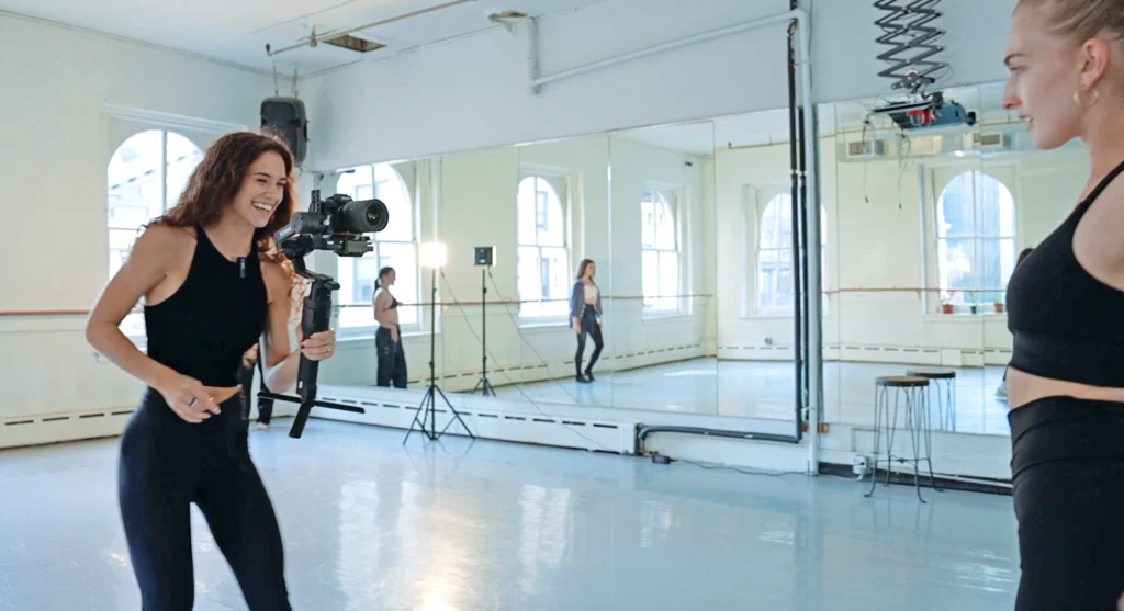 Elsa Stallings films a dancer in a studio while holding a camera and stabilizer.