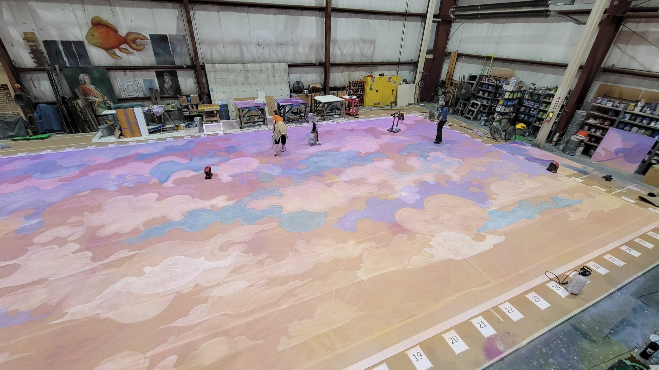 Backstage, stagehands and artists work on painting a massive cloudscape backdrop.