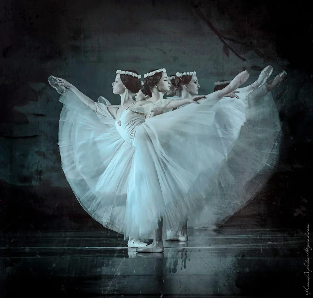 A line of female corps de ballet dancers dressed as sylphs stand in arabesque, one behind the other.