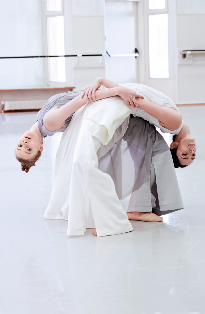 Lara Wolter and Julia Weiss hold each other's hands and stand hip-to-hip as they bend backward, heads almost touching the floor.