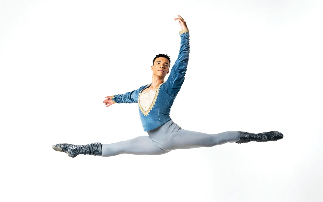 Fábio Mariano performs a saut de chat. He is wearing a blue and gray costume with dark gray boots.