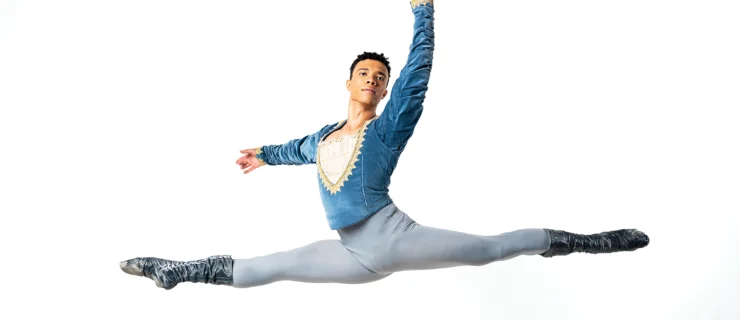 Fábio Mariano performs a saut de chat. He is wearing a blue and gray costume with dark gray boots.