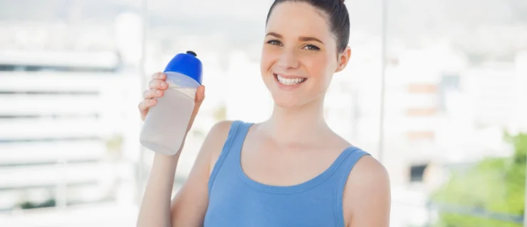 A young woman in a blue shirt smiles and poses with a reusable water bottle, her brown hair pulled into a bun.