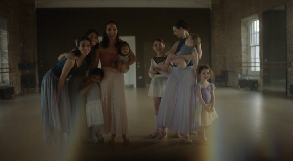 A still from "Colliding Forces: Mothers in Ballet" shows a group of ballerinas with their young children standing in a dance studio.